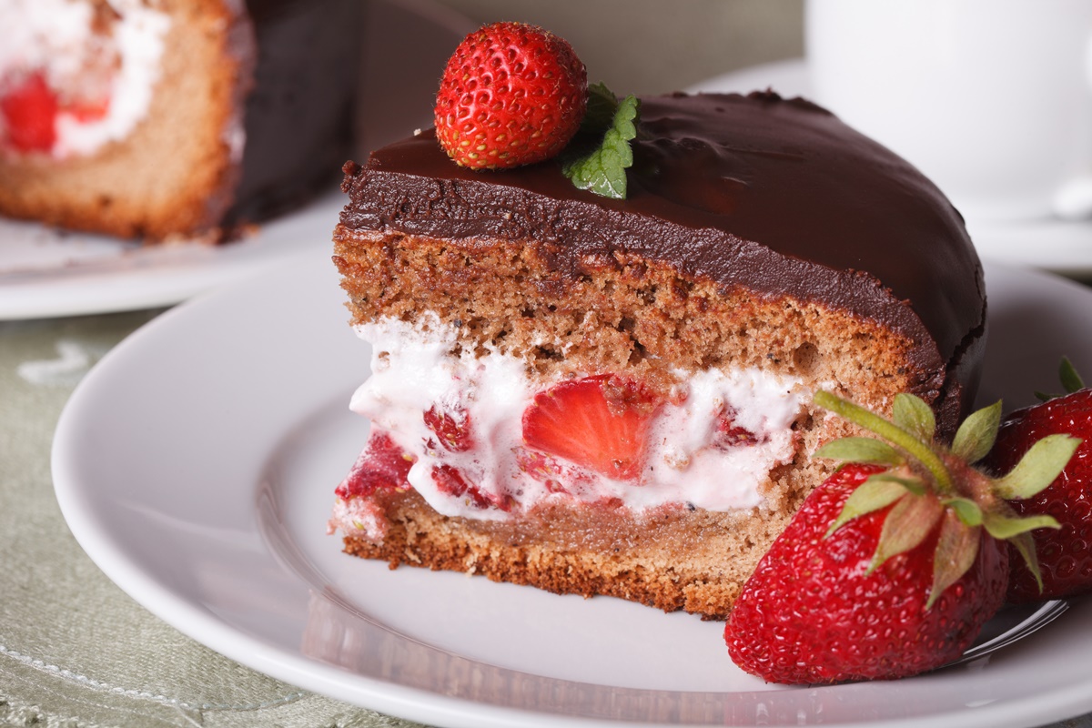 Porție de tort cu mousse de căpșuni și glazură de ciocolată pe o farfurie albă