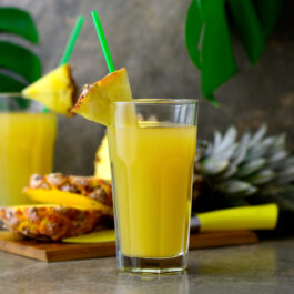 Suc de ananans într-un pahar transparent cu un pai verde
