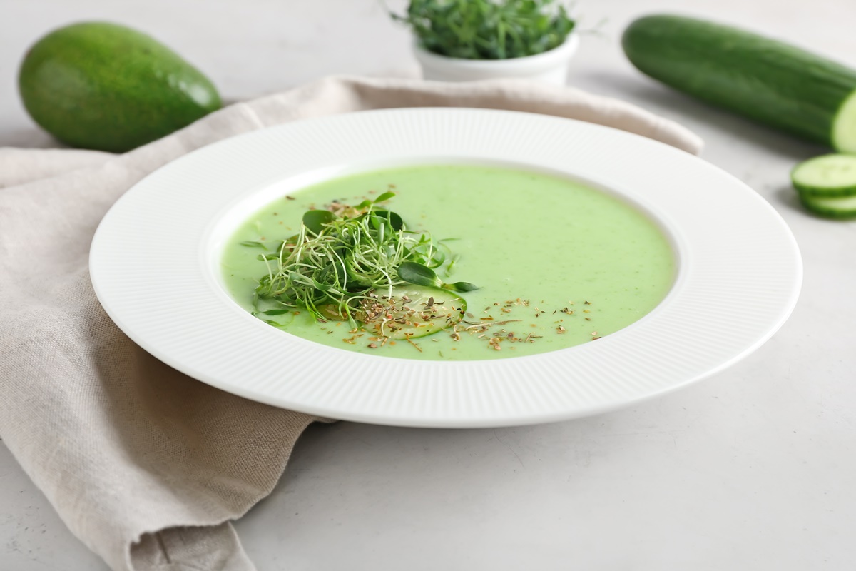 Supă rece de avocado cu castravete în farfurie albă, decorată cu verdeață
