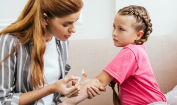O mamă care pune un bandaj pe mână fiicei sale pentru a ilustra cum tratăm rănile superficiale la copii