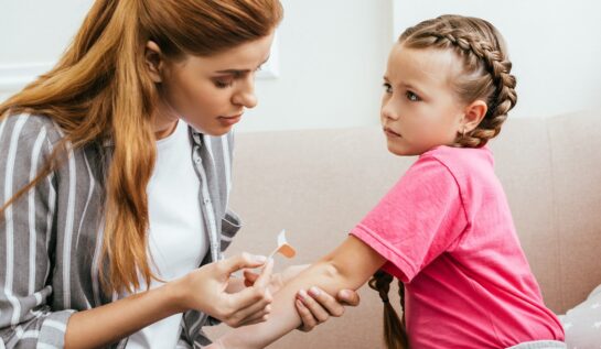 O mamă care pune un bandaj pe mână fiicei sale pentru a ilustra cum tratăm rănile superficiale la copii