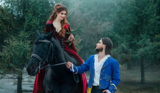 Un cuplu de îndrăgostiți cu o prințesă în rochie roșie care stă pe un cal negru în timp ce jos o așteaptă un prinț într-un costum albastru pentru a reprezenta acele zodii norocoase în dragoste pe data de 23 iunie 2022