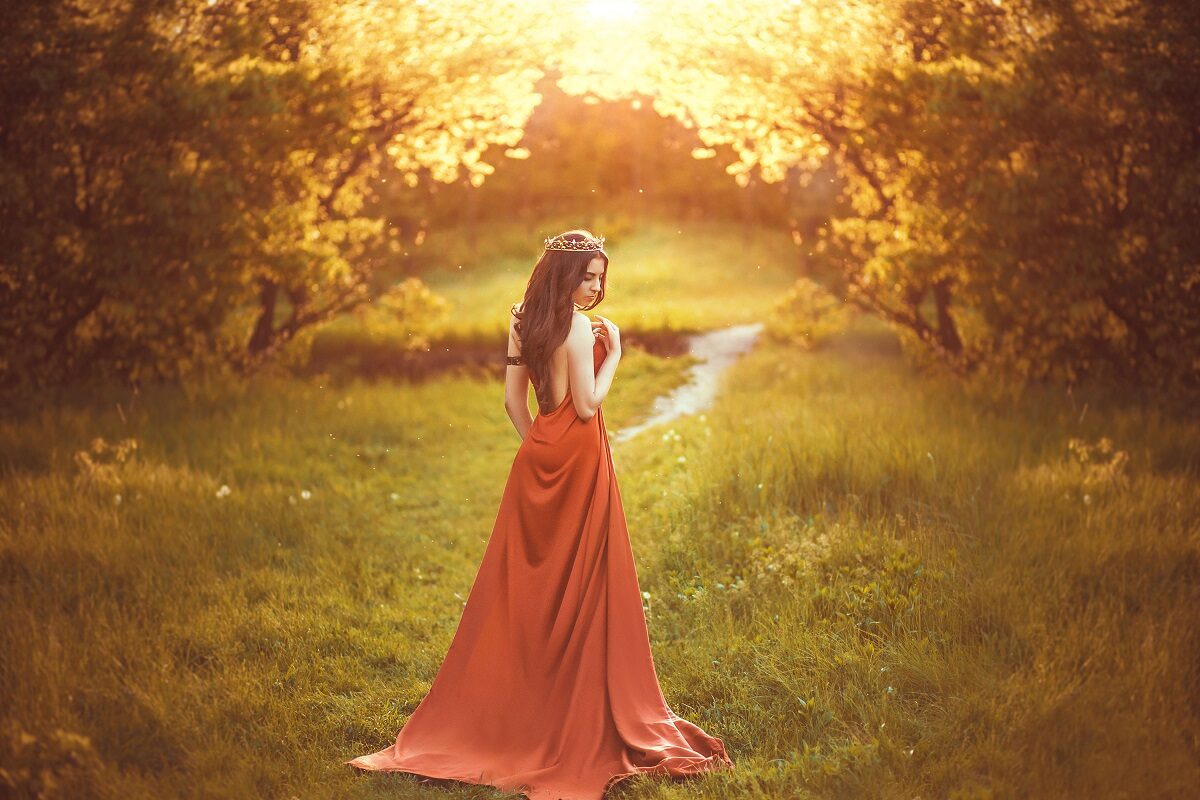 O femeie frumoasă care poartă o rochie roșie și stă într-o pădure pentru a reprezenta una din zodiile care se despart pe data de 26 iunie 2022