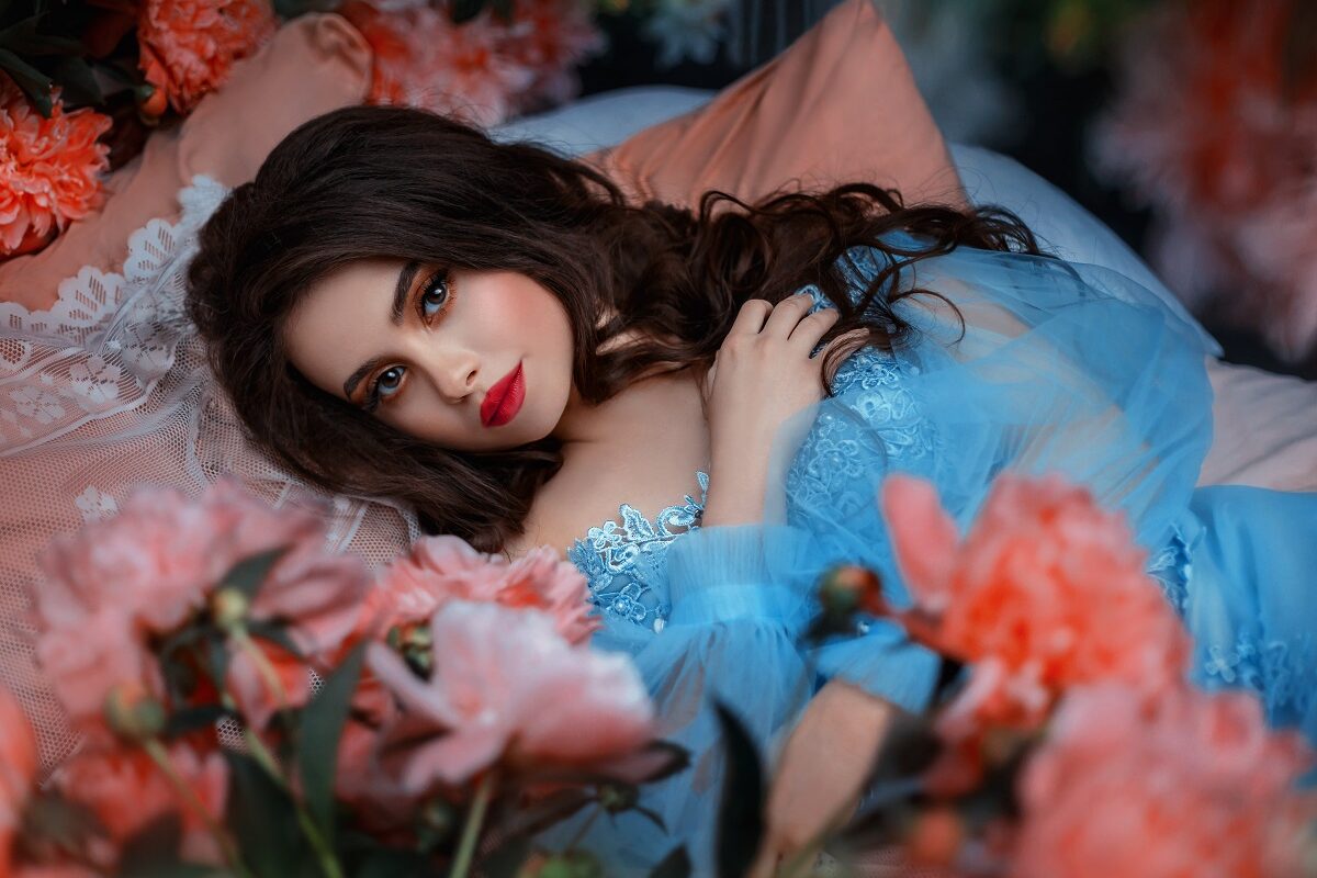O femeie frumoasă într-o rochie albastră care stă pe un pat de flori pentru a reprezenta una din cele trei zodii norocoase în dragoste pe data de 27 iunie 2022