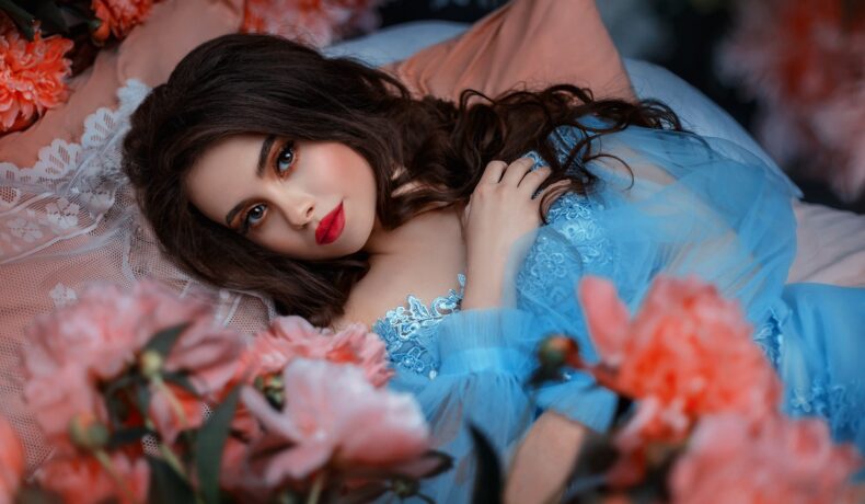 O femeie frumoasă într-o rochie albastră care stă pe un pat de flori pentru a reprezenta una din cele trei zodii norocoase în dragoste pe data de 27 iunie 2022