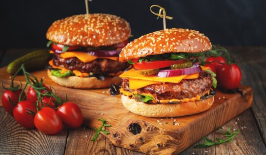 Un blat de lemn pe care se află doi burgeri pentru a ilustra unele dintre principalele alimente populare vara