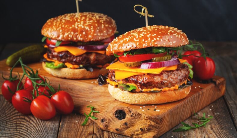 Un blat de lemn pe care se află doi burgeri pentru a ilustra unele dintre principalele alimente populare vara