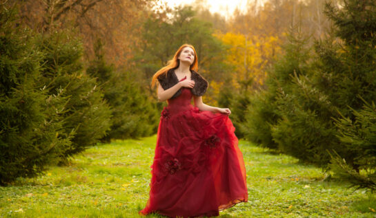 Fată frumoasă îmbrăcată într-o rochie lungă, roșie, stă într-o pădure