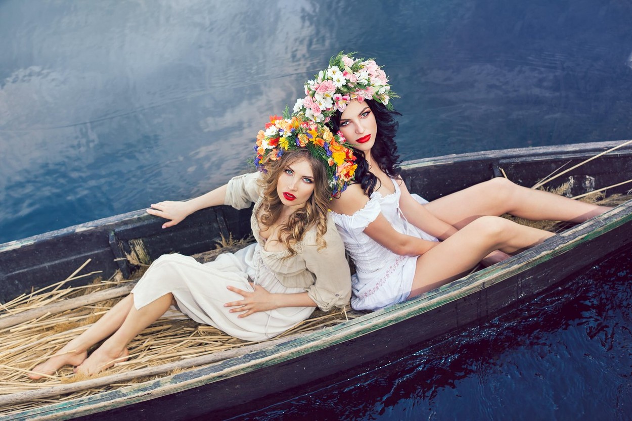 Două fete frumoase stau într-o barcă cu coroane de flori pe cap