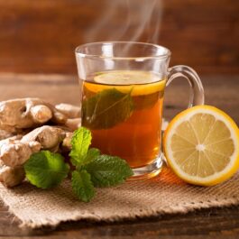 O masă pe care se află o carafă plină cu ceai alături de câteva rădăcini de ghimbir și o jumătate de lămâie pentru a ilustra unul din acele ceaiuri care te ajută să slăbești
