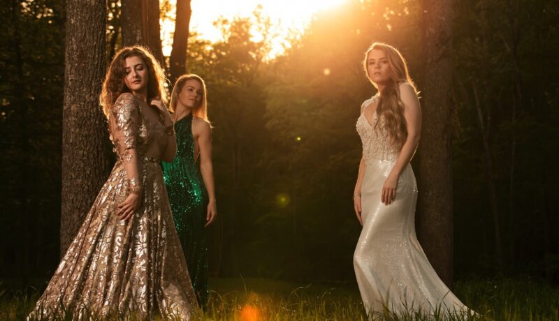 Trei femei frumoase care pozează la apus într-o pădure pentru a ilustra cum să accesorizezi o rochie de seară elegantă