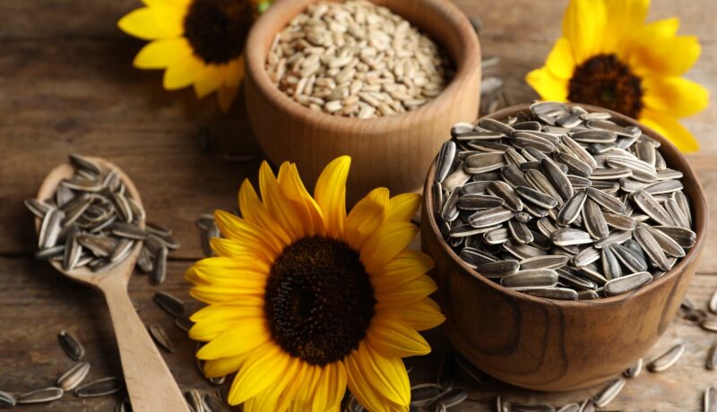 O masă de lemn pe care se află flori de floarea-soarelui și semințe pentru a ilustra efectele consumului de semințe de floarea-soarelui