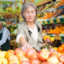 O femeie care alege din piață câteva fructe care sunt recomandate după vârsta de 50 de ani