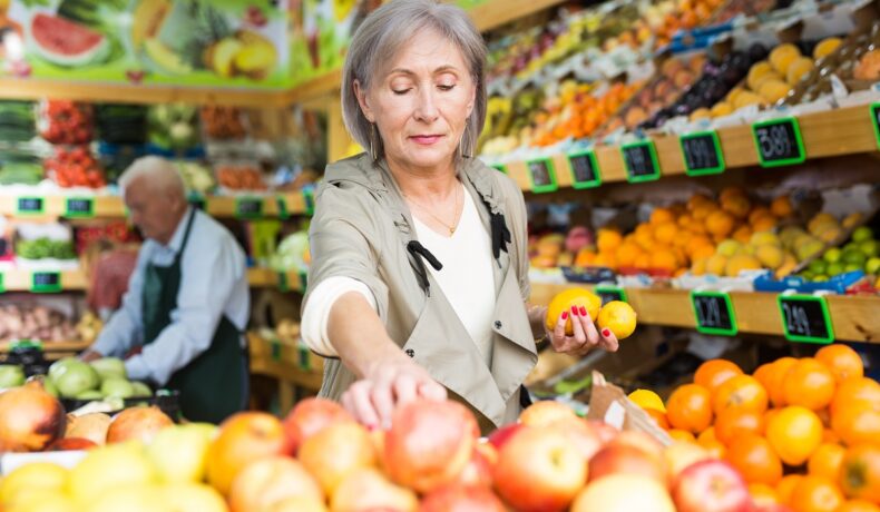 O femeie care alege din piață câteva fructe care sunt recomandate după vârsta de 50 de ani