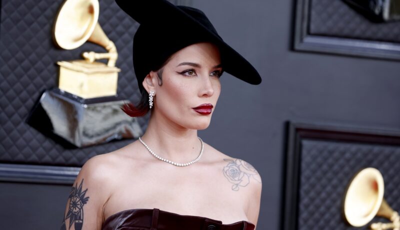 Halsey îmbrăcată într-o rochie cu umerii goi și o pălărie elegantă în timp ce pozează la Gala Premiilor Grammy 2022