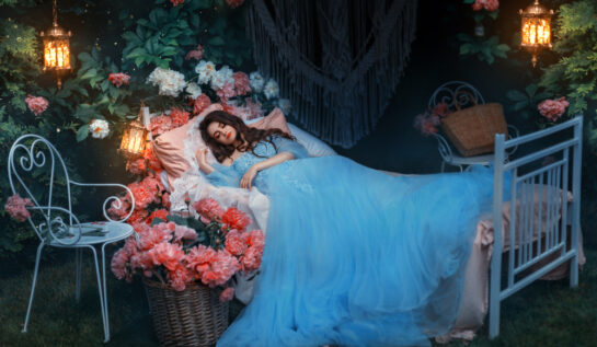 Fată frumoasă îmbrăcată într-o rochie albastră lungă stă întinsă într-un pat