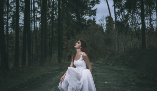 Fată frumoasă îmbrăcată într-o rochie albă în pădure