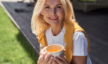 O femeie de 50 de ani care bea ceai dintr-o ceașcă albă, în natură
