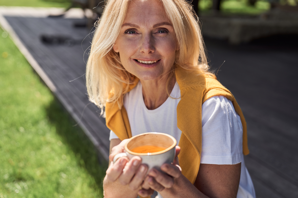O femeie de 50 de ani care bea ceai dintr-o ceașcă albă, în natură