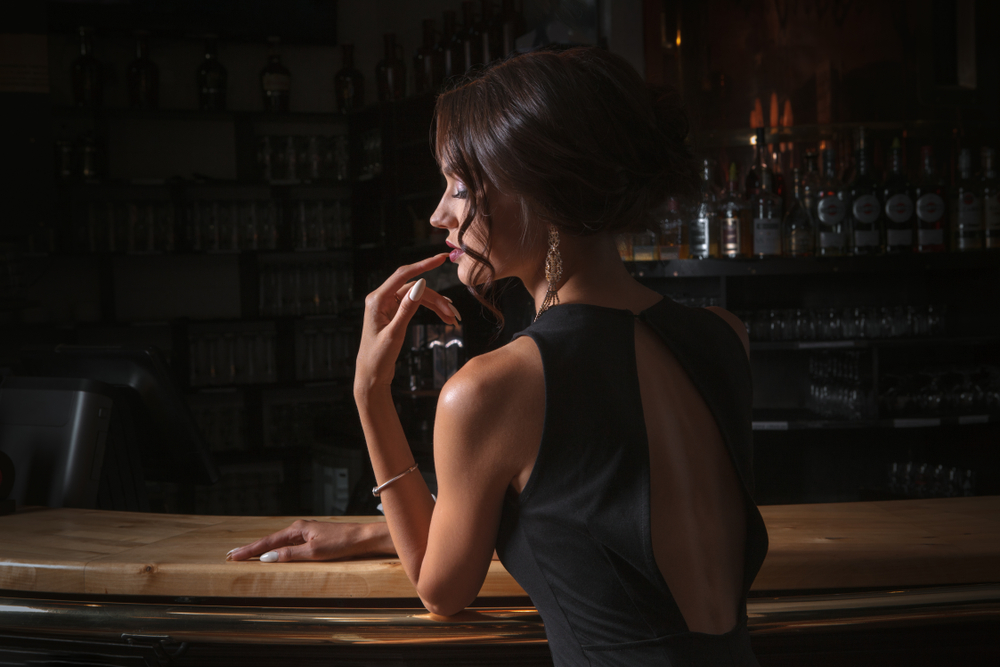 O femeie timidă, la un bar, într-o rochie elegantă
