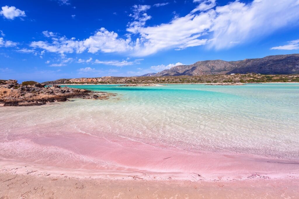 Panoramă care ilustrează o plajă cu nisipul roz, plaha Elafonissi din Grecia