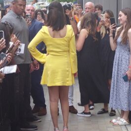 Selena Gomez cu spatele într-o rochie galbenă în timp ce pozează pentru admiratorii săi