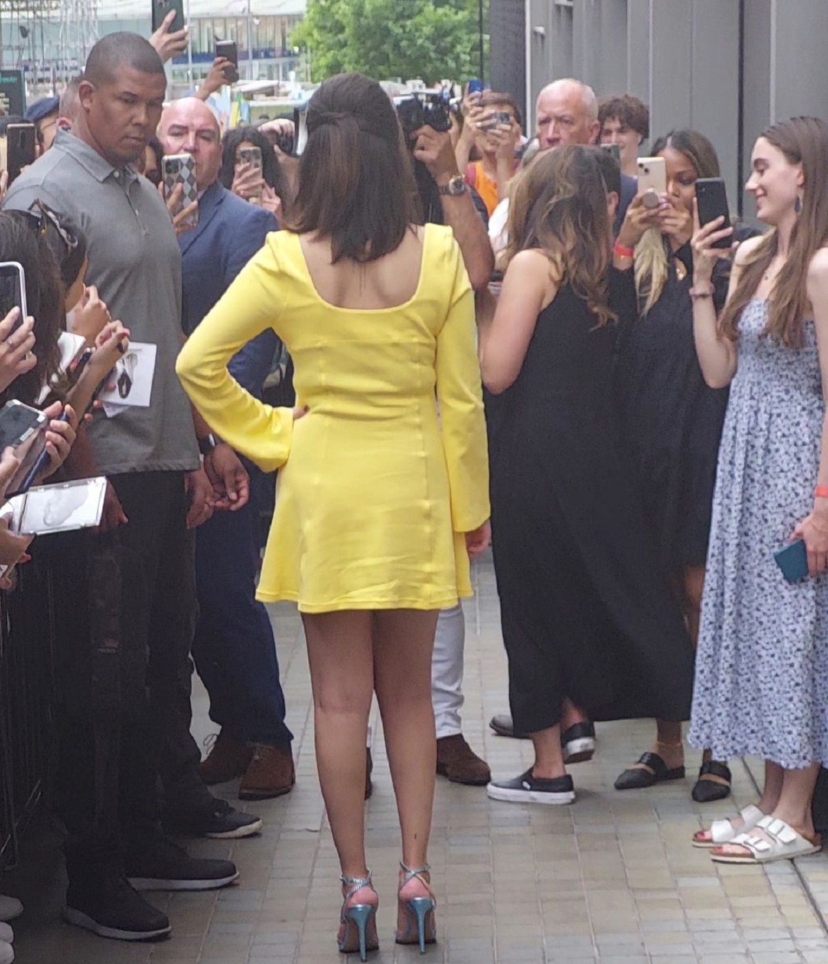 Selena Gomez cu spatele într-o rochie galbenă în timp ce pozează pentru admiratorii săi