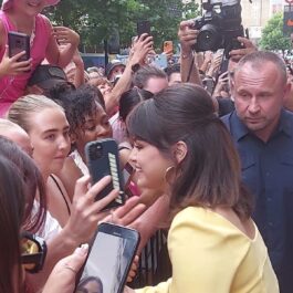 Selena Gomez într-o rochie galbenă în timp ce vorbește cu fanii dn mulțime în fața unui hotel din Londra