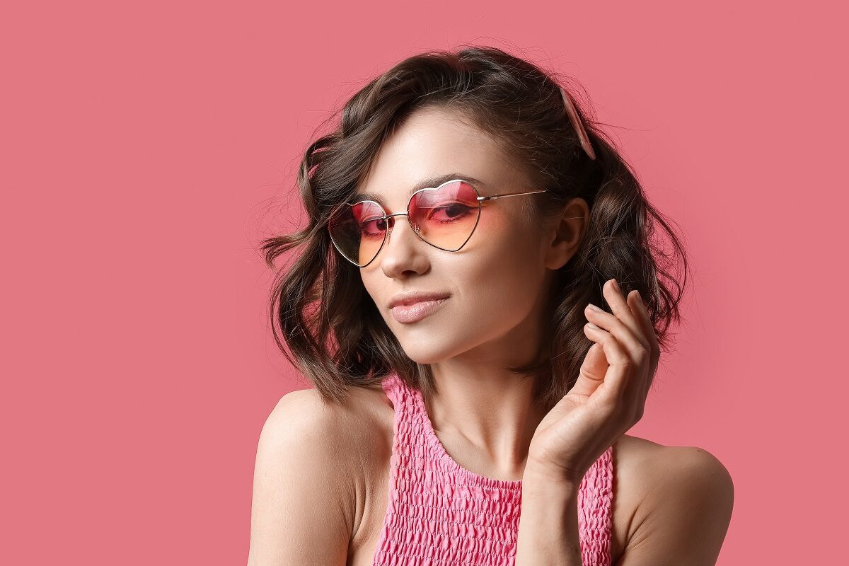 O femeie frumoasă care poartă o bluză roz și o pereche de ochelari de soare roz în timp ce își aranjează părul care este pe lista de tunsori bob care sunt în trend în 2022