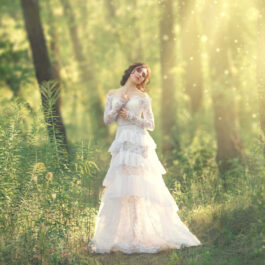 Fată frumoasă îmbrăcată în alb stă în picioare într-o pădure