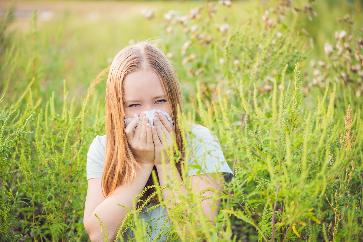 O femeie blondă care stă într-un câmp în timp ce își suflă nasul de alergia la ambrozie