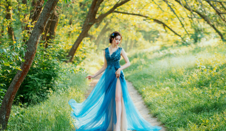 Fată frumoasă îmbrăcată într-o rochie lungă, albastră merge prin pădure