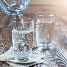 Două pahare cu apă care stau pe un blat de lemn pentru a ilustra care este cea mai bună băutură pentru a pierde în greutate