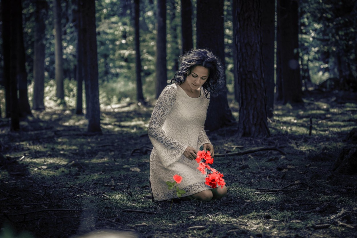 Fată frumoasă îmbrăcată în rochie albă de mireasă stă pe jos într-o pădure
