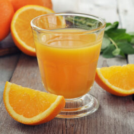 Suc de portocale, într-un pahar din sticlă, cu felii de portocale alături
