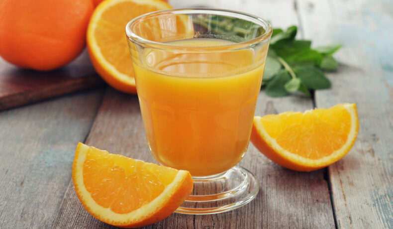 Suc de portocale, într-un pahar din sticlă, cu felii de portocale alături