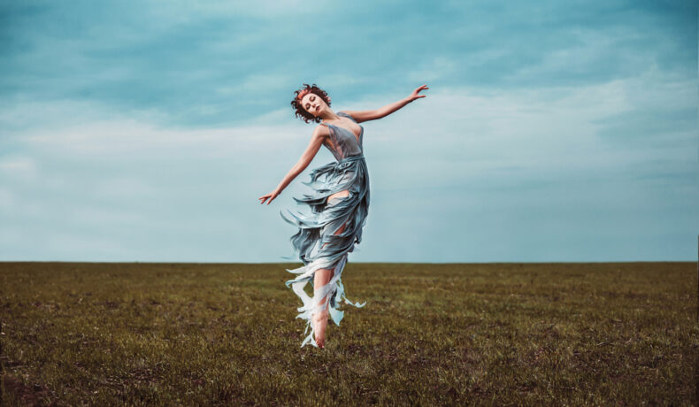 Fată frumoasă îmbrăcată într-o rochie lungă dansează în aer