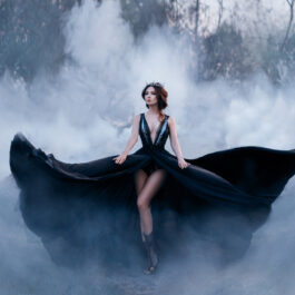 Fată frumoasă îmbrăcată într-o rochie neagră lungă stă în pădure