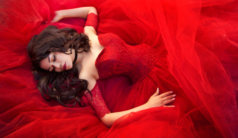 Fată frumoasă îmbrăcată în roșu stă pe o pătură roșie ca focul