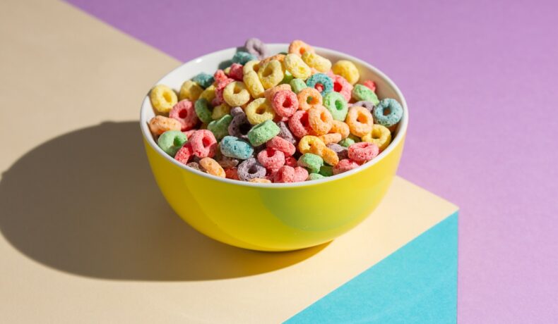 O masă roz pe care se află un bol cu cereale obținute cu ajutorul coloranților alimentari care ar putea fi periculoși pentru sănătatea ta