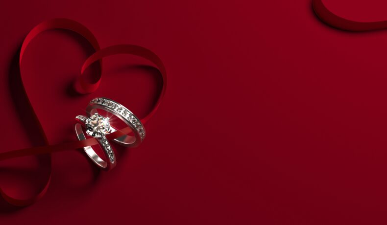 O imagine cu fundal roșu pe care se află un inel de logodnă și o verighetă pentru a ilustra e recomandat să porți inelul de logodnă în ziua nunții