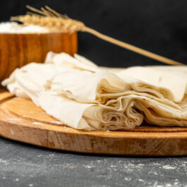 Foi de plăcintă cu ulei și oțet, așezate pe un suport din lemn, alături de un bol în care se află făină de grâu.