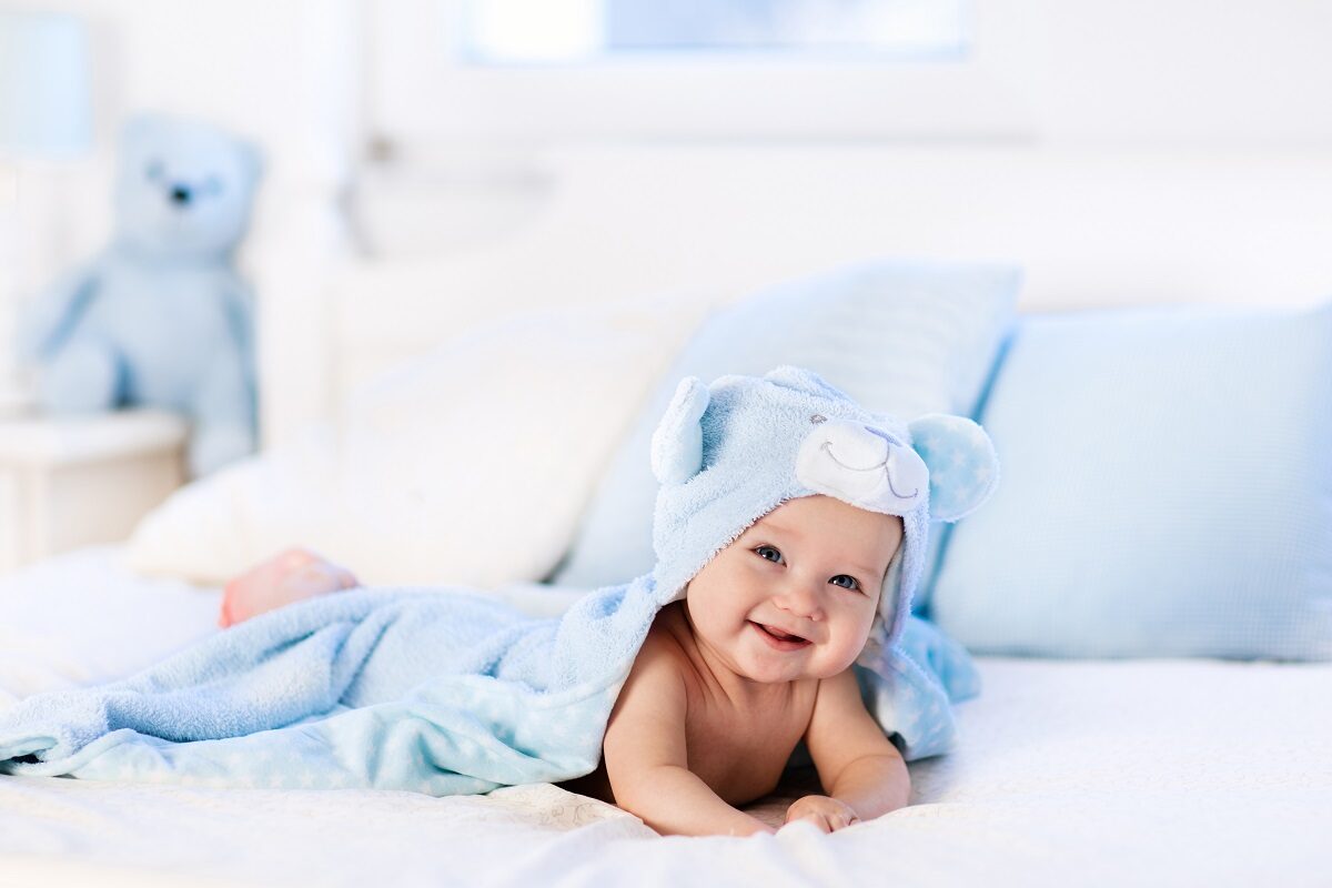Un bebeluș care stă într-un pat și zâmbește în timp ce vrea să ilustreze care sunt cele mai neobișnuite nume de copii în anul 2022