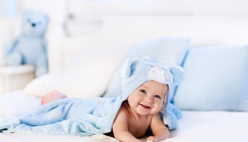 Un bebeluș care stă într-un pat și zâmbește în timp ce vrea să ilustreze care sunt cele mai neobișnuite nume de copii în anul 2022