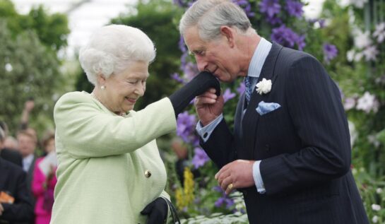 Regina Elisabeta în timp ce întinde mâna pe care i-o sărută fiul său, Prințul Charles