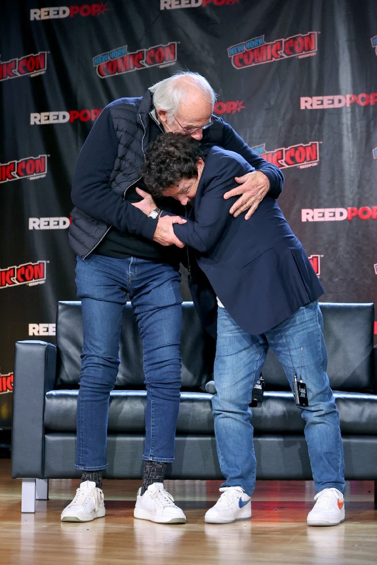 Michael J. Fox şi Christopher Lloyd în timp ce se îmbrățișează pe scena de la Comic Con New York 2022