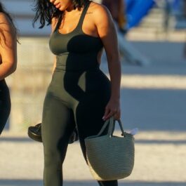 Chaney Jones într-un costum negru în timp ce merge pe o plajă din Miami