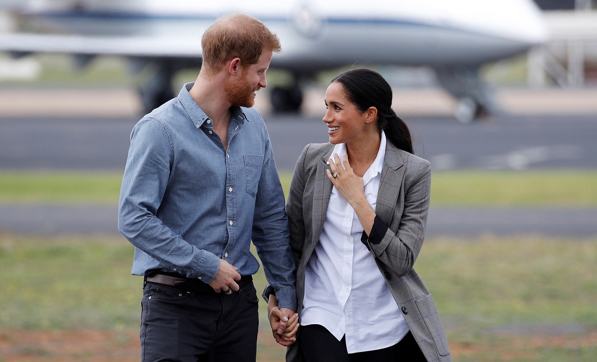 Meghan Markle și Prințul Harry în timp ce se țin de mână în fața unui avion după ce au aterizat în Australia, în cadrul unei vizite oficiale din 2018
