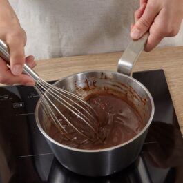 Femeie amestecând cu un tel în cratița cu glazură de ciocolată