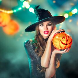 O femeie frumoasă care ține în mână un dovleac și pozează într-unul din principalele costume de Halloween făcute acasă